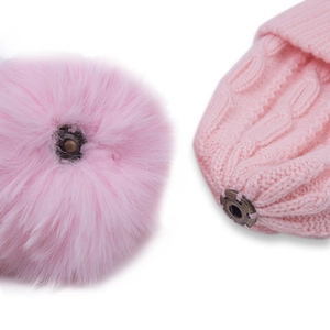 Pink knitted baby hat with a detachable faux fur pompom and metal snap fastener detail