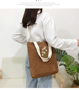 Detail of brown corduroy tote bag with white daisy embroidery and beige shoulder strap