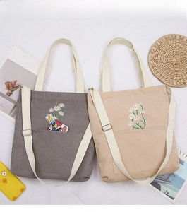 Close-up of daisy embroidery on corduroy tote bag showing spacious front pocket and texture