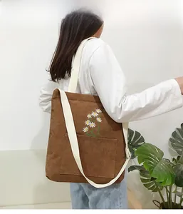 Detail of daisy embroidery on brown corduroy tote bag with wide white shoulder strap
