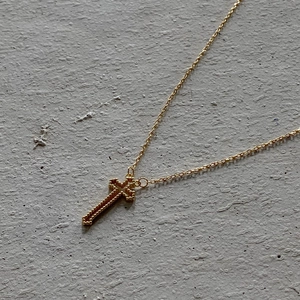 Close-up of gold cross pendant with beaded texture and fine chain on stone
