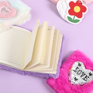 Three colorful plush unicorn notebooks with sequin hearts and lined paper displayed on purple
