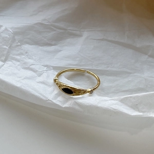 Detail view of gold open ring with black evil eye inlay on textured white paper