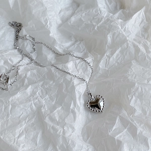 Detailed view of a silver heart pendant necklace with a beaded edge on a white paper background