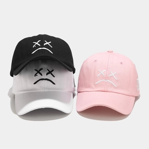 Detalle de gorras de algodón con bordado de cara triste en colores negro, rosa y blanco