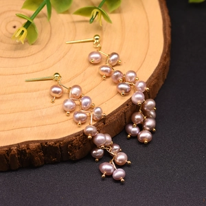Detailed macro shot of long 18k gold-plated pearl tassel earrings on a wooden background