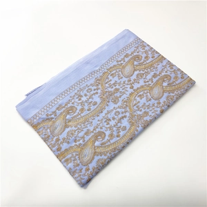Detailed view of light blue cashmere-like shawl with golden paisley embroidery and tassels