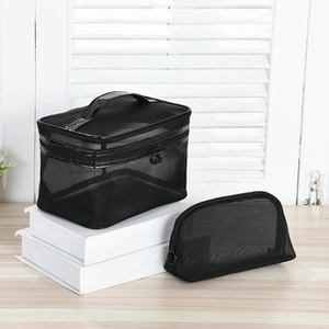 Close-up of black mesh makeup bags with top handles and zippers on white books