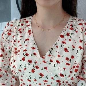 Detailed view of minimalist gold leaf pendant necklace worn on neck with floral dress