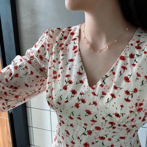 Detail of a gold leaf charm necklace worn by a model on a dainty chain link