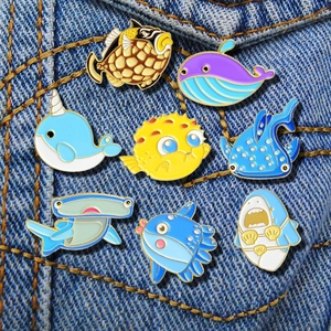 Collection of eight colorful ocean animal enamel pins pinned on blue denim fabric