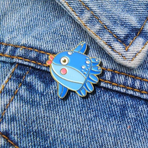 Macro shot of cute enamel ocean sunfish pin with gold metal edges on denim fabric