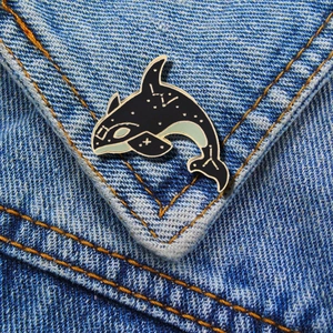 Detailed view of an orca enamel pin with gold constellations on blue denim fabric