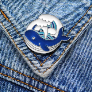 Detail of round whale and sea wave enamel pin attached to blue denim fabric