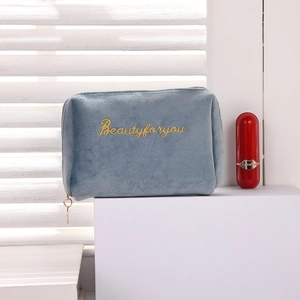Blue velvet cosmetic bag with gold embroidery shown on white cube with lipstick
