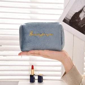 Detail of blue velvet makeup bag featuring gold embroidery and soft texture in hand