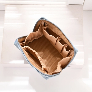 Top view of open denim makeup bag showing brown lining and multiple elastic compartments