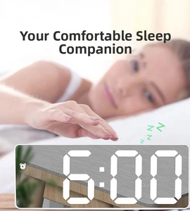 Digital LED mirror alarm clock displaying 6:00 AM with a sleeping person in background