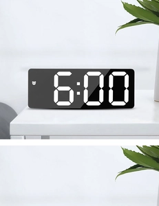 Macro shot of rectangular black LED mirror alarm clock showing 6:00 on white desk