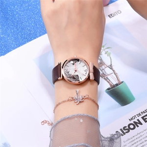 Close-up of rose gold watch with brown leather strap and maple leaf pendant bracelet