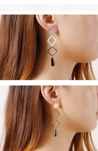 Close-up of geometric drop earrings with layered diamond frames and black teardrop beads