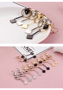 Detail view of heart and square metal pendant earrings in black, gold, and silver finishes