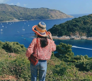 Colorful crochet sun hat paired with a red floral shirt against a scenic coastal backdrop