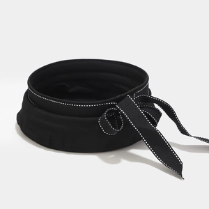 Detailed close-up of a black canvas hat with white contrast stitching and adjustable bow tie