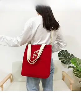 Detail of red corduroy tote bag featuring daisy embroidery and wide cream shoulder strap