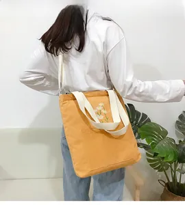 Daisy embroidered yellow corduroy tote bag shown on model with white woven straps