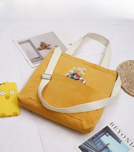 Detail of yellow corduroy tote bag featuring daisy embroidery and adjustable strap