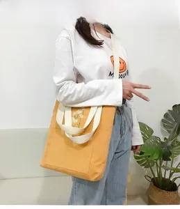 Close-up of yellow corduroy tote bag with embroidered daisies and front pocket detail