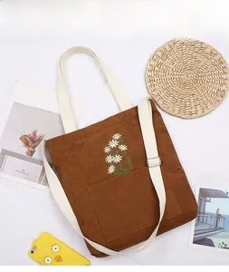 Detailed close-up of brown corduroy tote bag with white daisy embroidery and front pocket