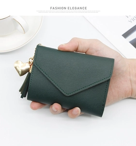 Detail of dark green small wallet with gold heart pendant and tassel held in hand