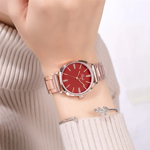 Close-up of a red dial watch with rose gold strap and silver leaf bracelet on a wrist