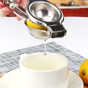 Manual stainless steel lemon squeezer pressing fresh juice into a white cup in a kitchen