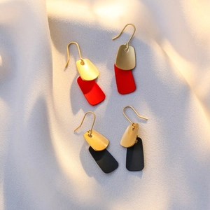 Close-up of matte geometric dangling earrings in red and black gold on soft fabric