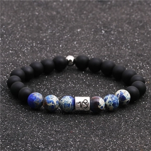 Detailed view of Capricorn zodiac charm on matte black beads and blue stone bracelet