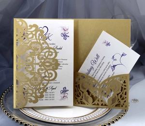 Detail of laser-cut gold lace wedding invitation with elegant floral inserts on a plate