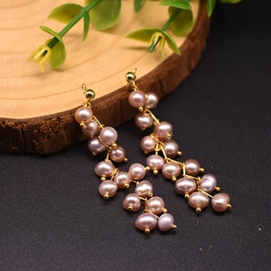 Detailed close-up of long 18k gold pearl drop earrings on a natural wooden display