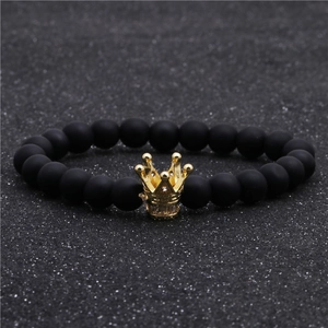 Gros plan d'un bracelet en perles noires mates avec un pendentif couronne dorée et zircons