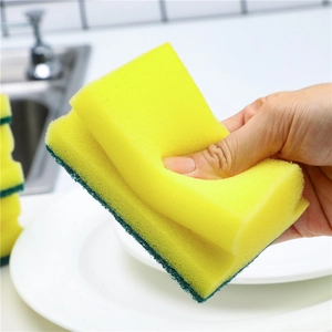 Dual-sided kitchen sponge with yellow foam and green scouring pad held in hand for cleaning