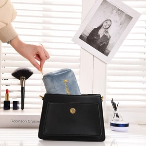 Blue velvet makeup bag with gold embroidery shown being taken out of a black handbag