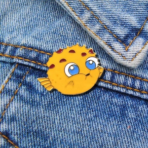 Detailed close-up of a yellow pufferfish enamel pin on a denim jacket pocket edge