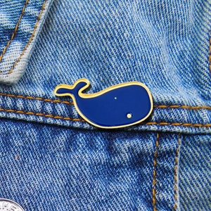 Detail view of a cute blue enamel whale brooch pinned on blue denim fabric texture