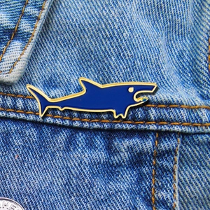 Detailed close-up of a dark blue enamel shark brooch with gold edges on denim fabric