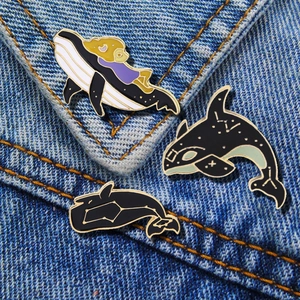 Three enamel whale brooches with moon and star patterns pinned on blue denim pocket