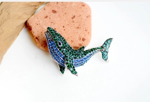 Detailed view of whale brooch with blue and green gradient rhinestones on stone