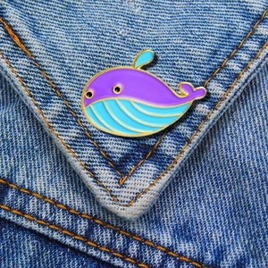 Detail of cartoon whale enamel brooch in purple and blue on denim background