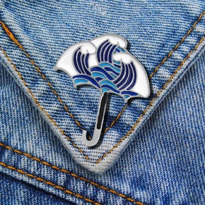 Detail of Great Wave enamel umbrella pin showing blue ocean waves on denim fabric
